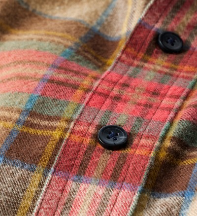 Close up detail shot of plaid flannel fabric with two black buttons, showcasing texture and pattern.