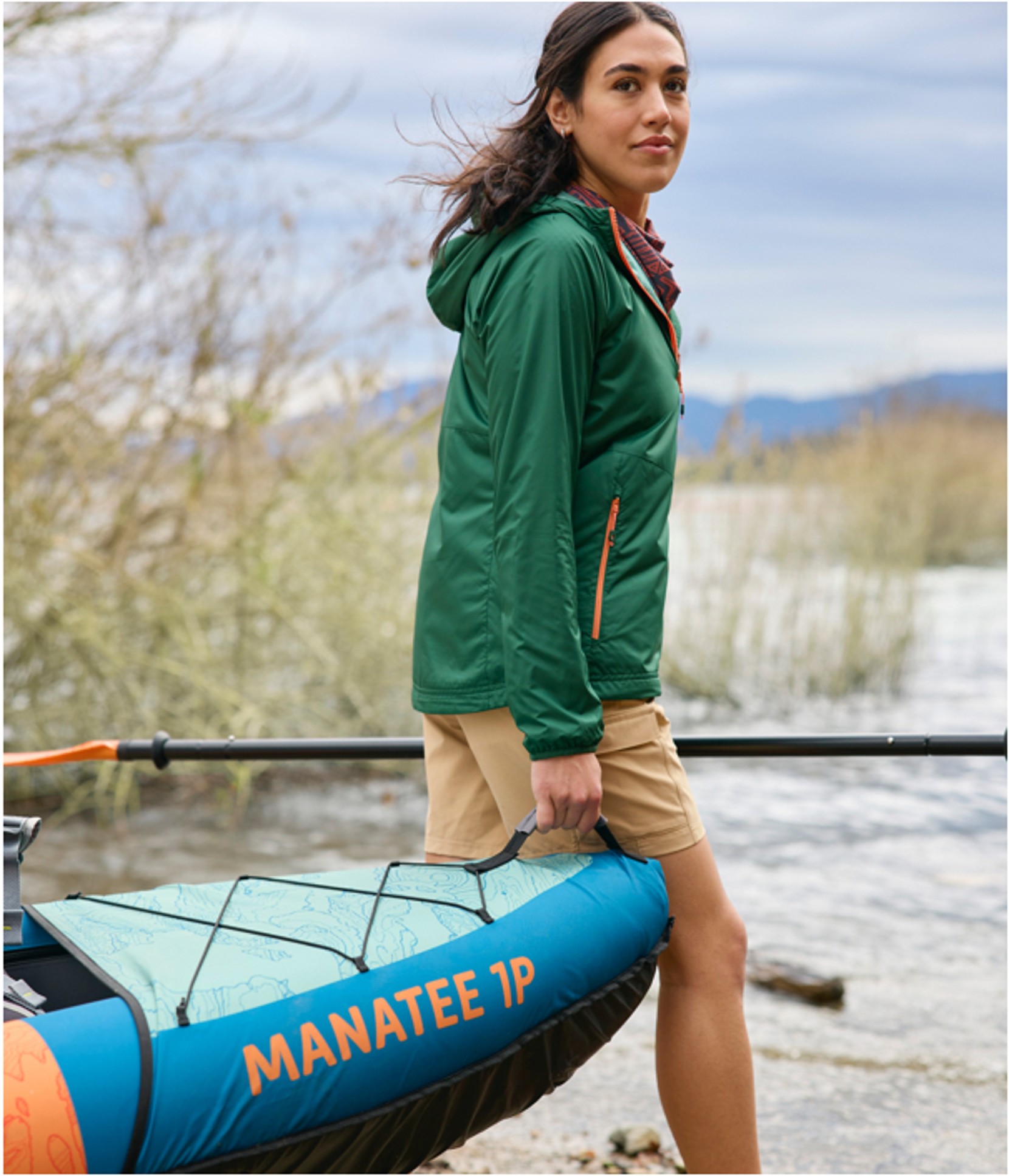 A woman walking on the beach carrying the front end of a Manatee Inflatable Kayak.