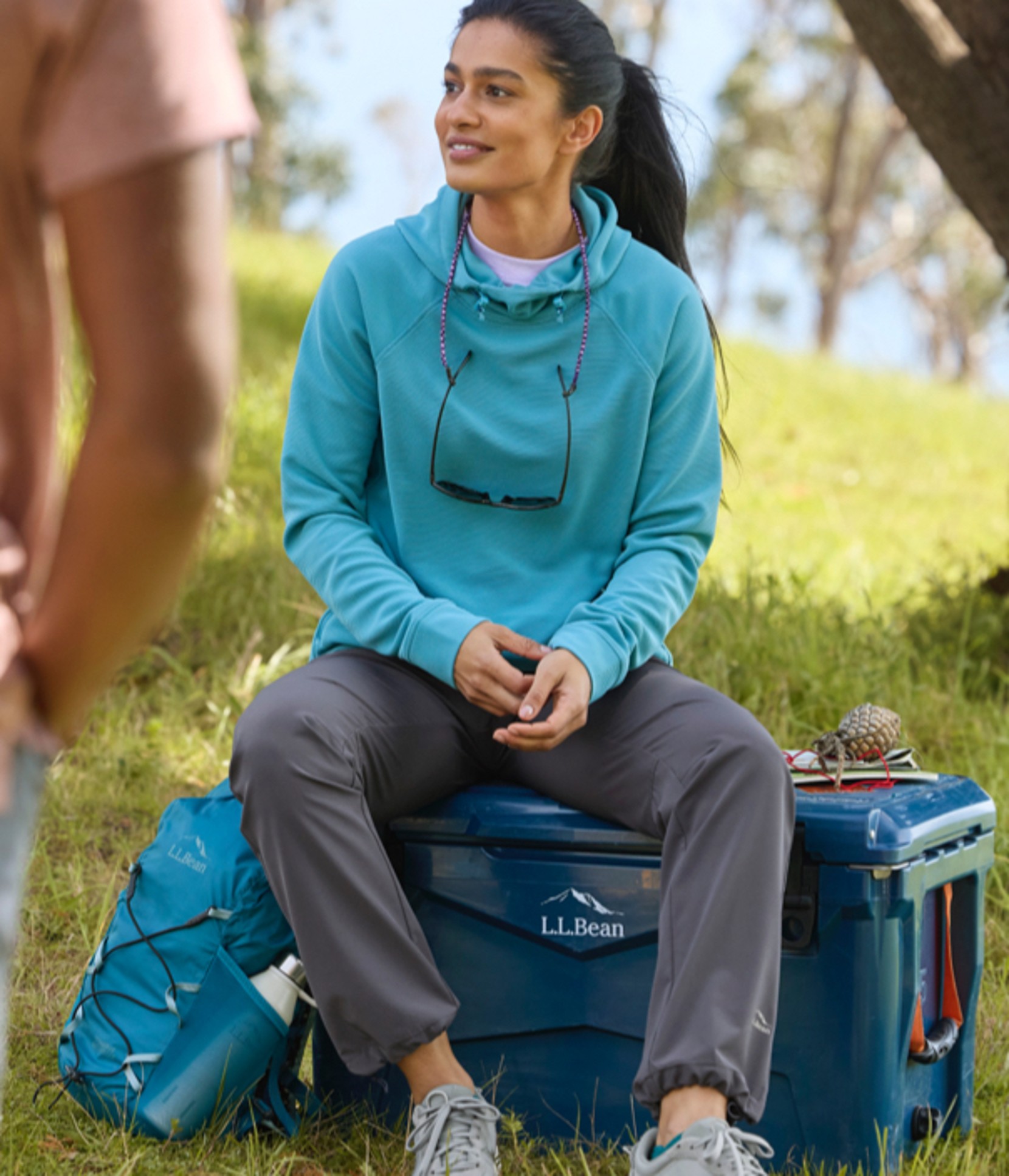 A person camping in the shade sitting on a blue cooler.