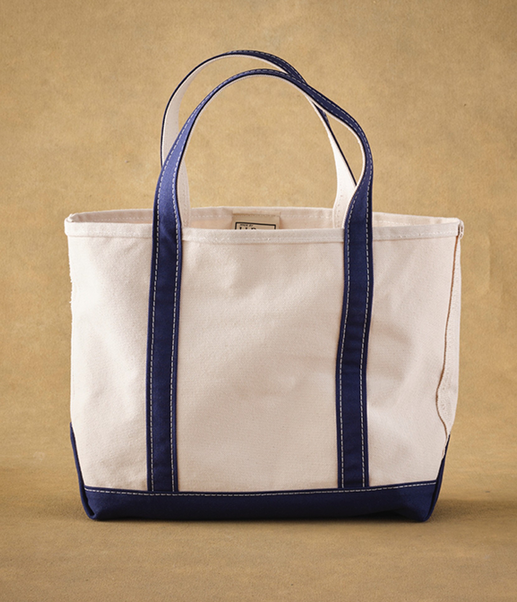 A durable, canvas L L Bean Boat and Tote with navy blue handles and trim against a tan background.