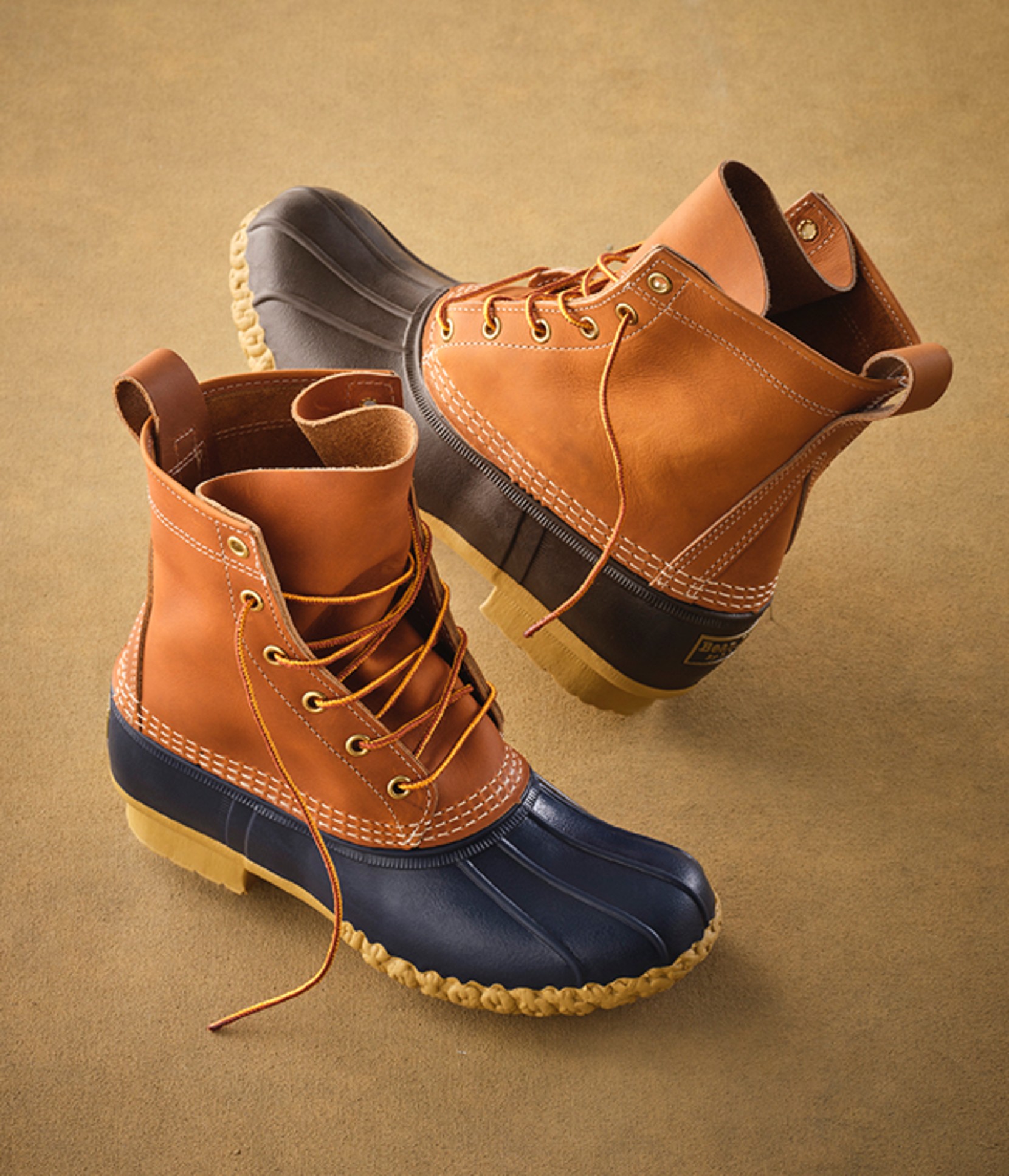 A pair of lace-up L L Bean boots on a beige background.