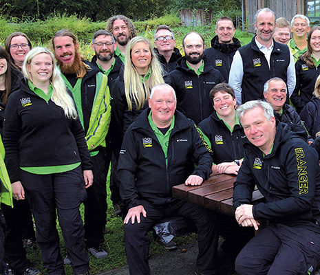 loch-lomond-trossachs-national-park-authority-large-group-of-staff-smiling-wearing-black-uniforms-and-green-shirts