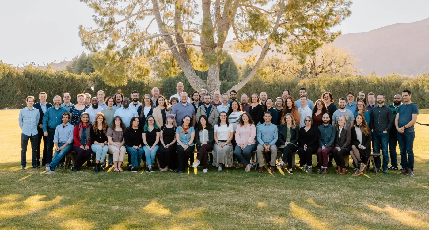 Team photo taken outdoors in the grass with a tree and mountains in the background.