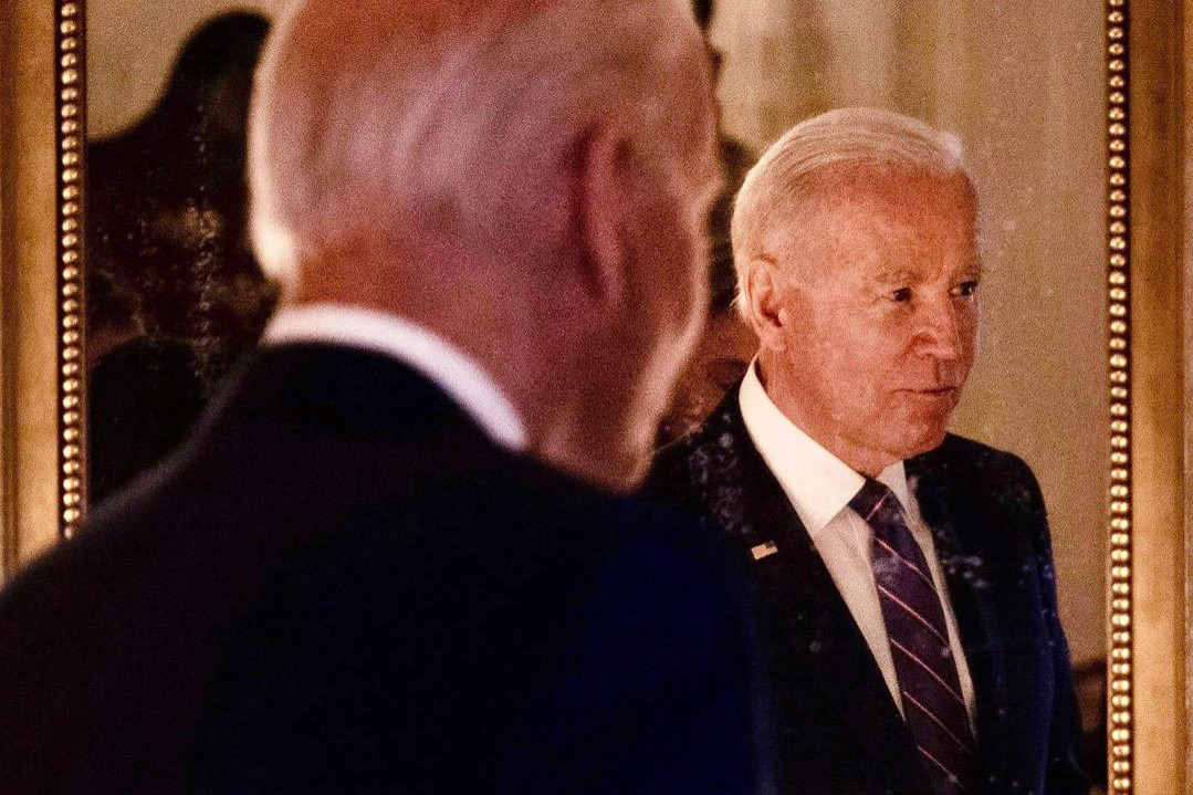 President Joe Biden stands, reflected in a mirror.