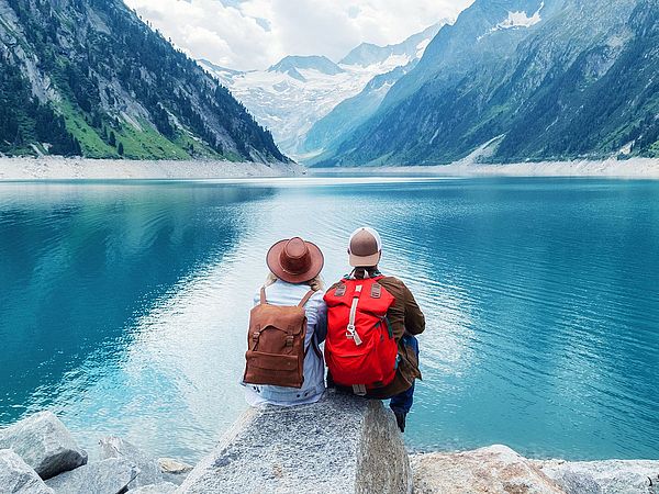 Ein Paar in Wanderkleidung sitzt auf einem Felsen und blickt auf einen See in den Bergen