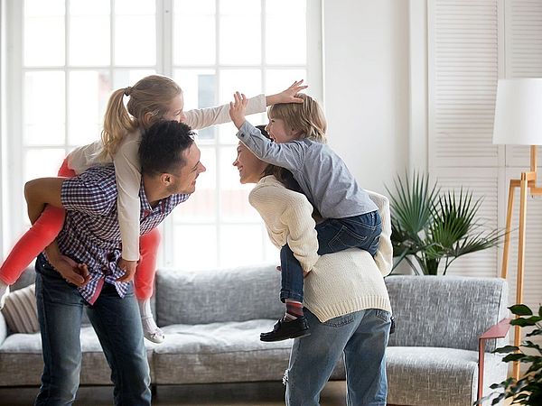 Die jungen glücklichen Eltern tragen ihre Kinder auf dem Rücken.