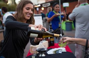 Person smiling and pouring a white wine for a guest