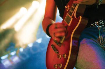 Closeup of person strumming guitar with floodlights in back