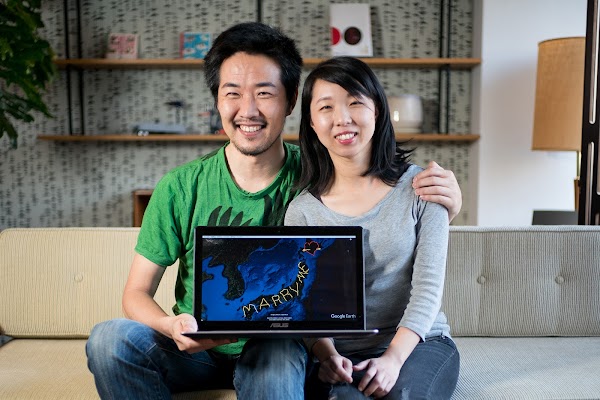 “Yassan” and his wife sit on a beige couch. They're holding a laptop that shows the GPS art that he used to propose to her.